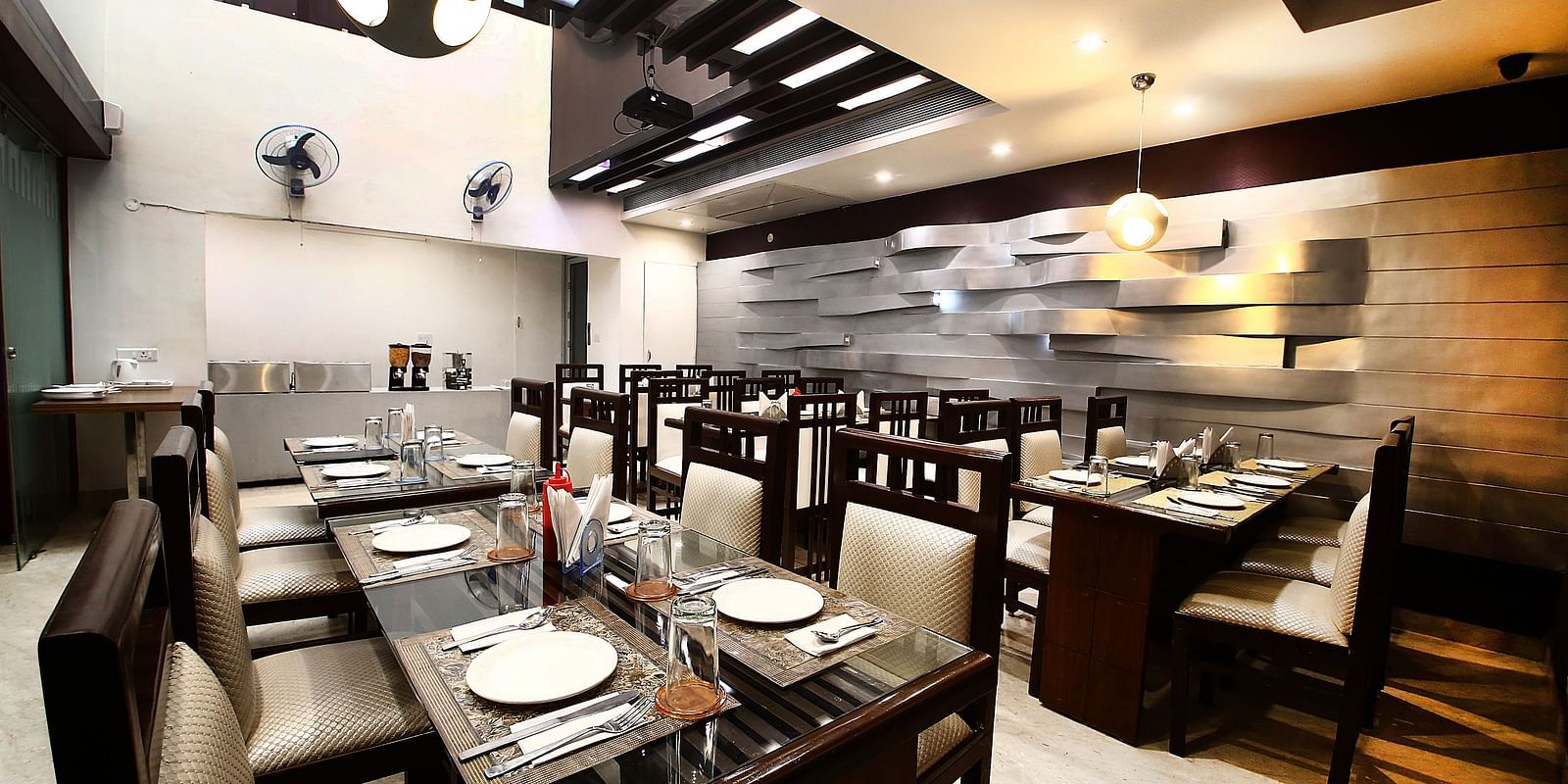 Dining space with various chairs and tables of beige and dark shades in a modern interior setting, detailed designing an textures on the walls and the ceilings - Hotel Emerald, Chandigarh
