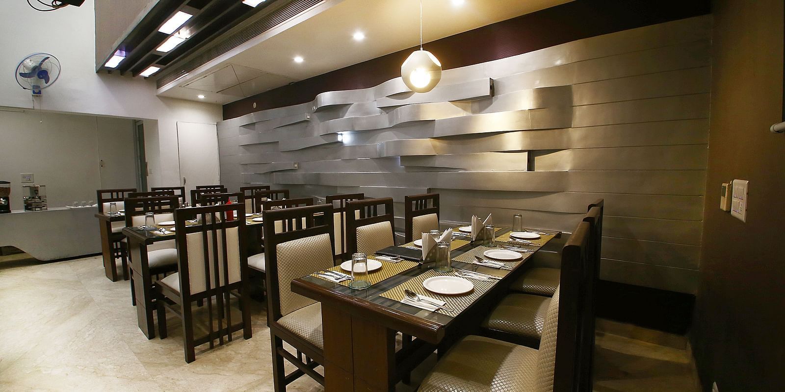 Uniformly placed chairs and tables of mocha and dark shades  in a modern light setting an extremely detailed walls and interior - Hotel Emerald, Chandigarh