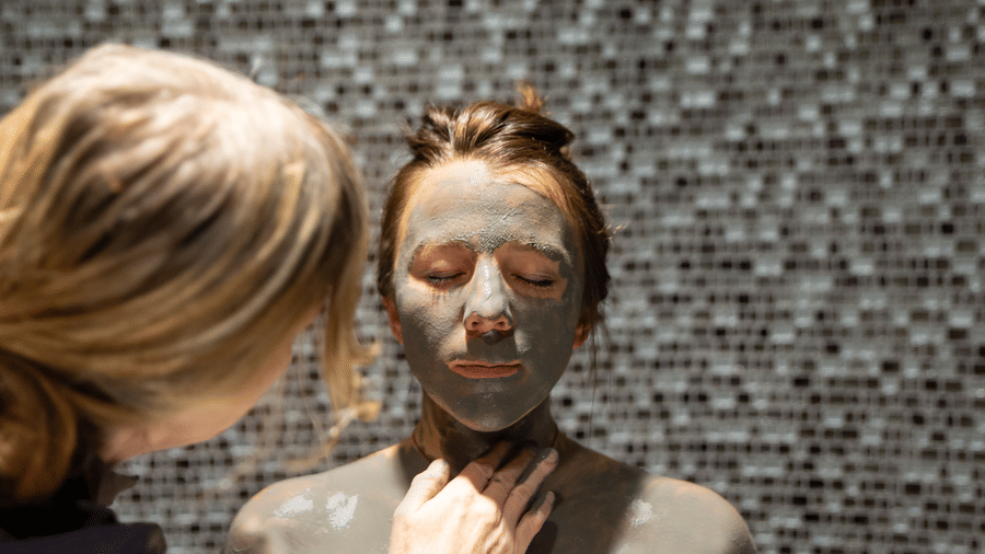 A therapist at YO1 Longevity Health Resorts Catskills applying mud to the face and body of a woman sitting with her eyes closed