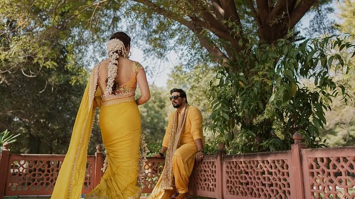 A woman walks gracefully towards a man sitting on a bench, surrounded by lush greenery and intricate architectural details. - Umaid Palace - A Lakeside Heritage Palace Resort