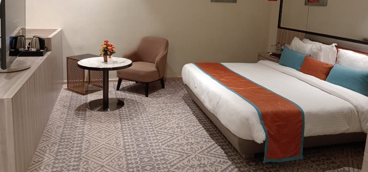 Modern hotel room with twin beds, a small table and chair, soft lighting, and minimalist decor.