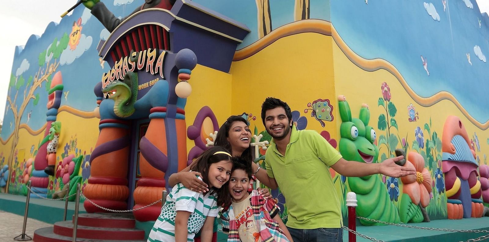 A happy family posing for a photo in front of a colorful cartoon-style mural at an amusement park, creating a cheerful and kid-friendly atmosphere - Ramoji Film City Hotels in Hyderabad 