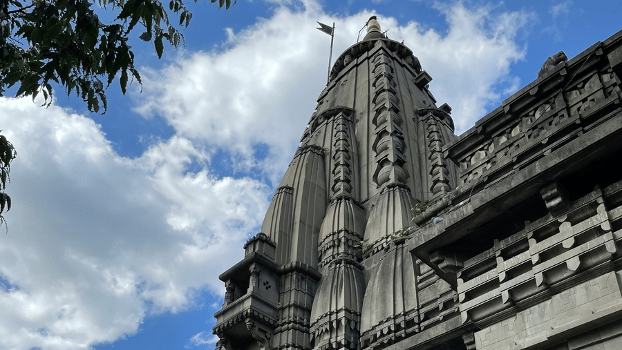 A stone temple structure with carved walls and a tall spire rising above the building against a blue sky.