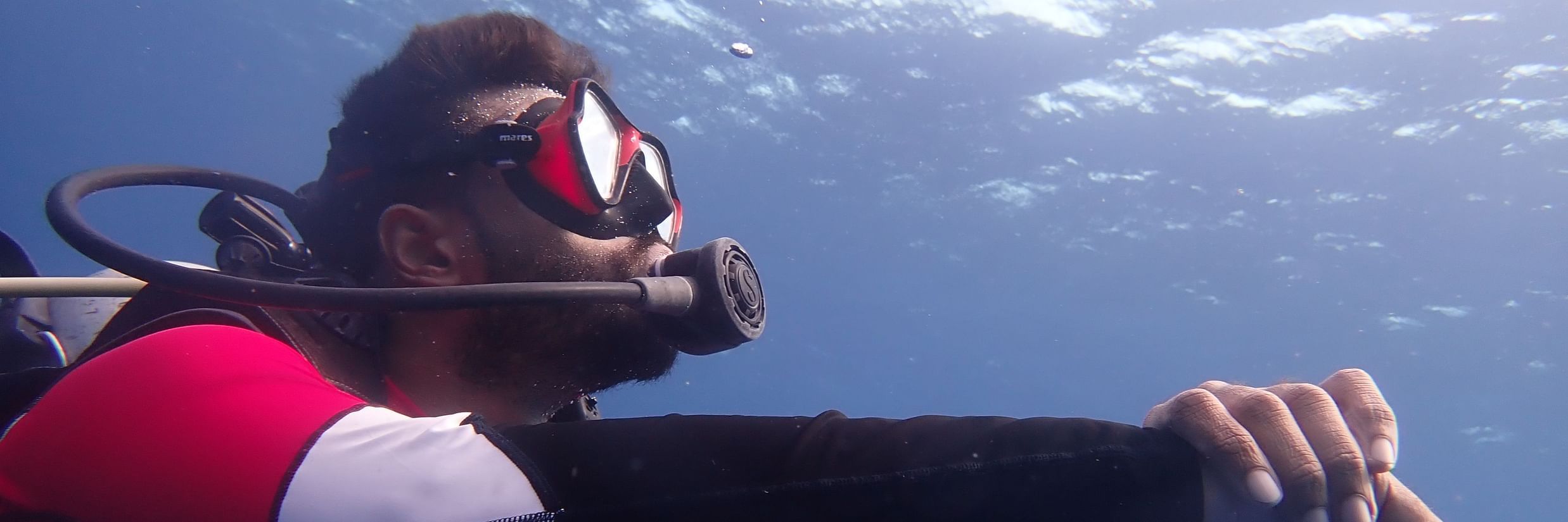 Barefoot Scuba Resort | Diver holding their wrist underwater, while surrounded by clear blue ocean water