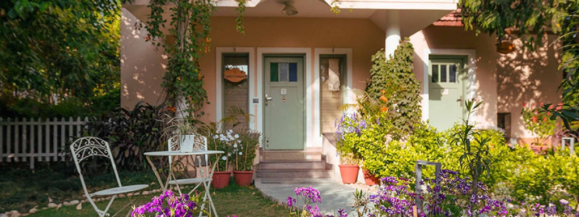 Rabbit Burrow at Karma Chalets with a small garden, outdoor chairs, flowers, and a white door with windows.