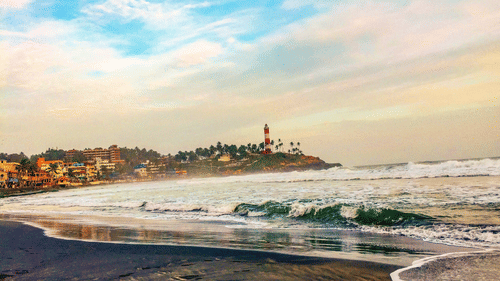 A view of a lighthouse beach where the waves are hitting the shore and it has a backdrop of a clear sky