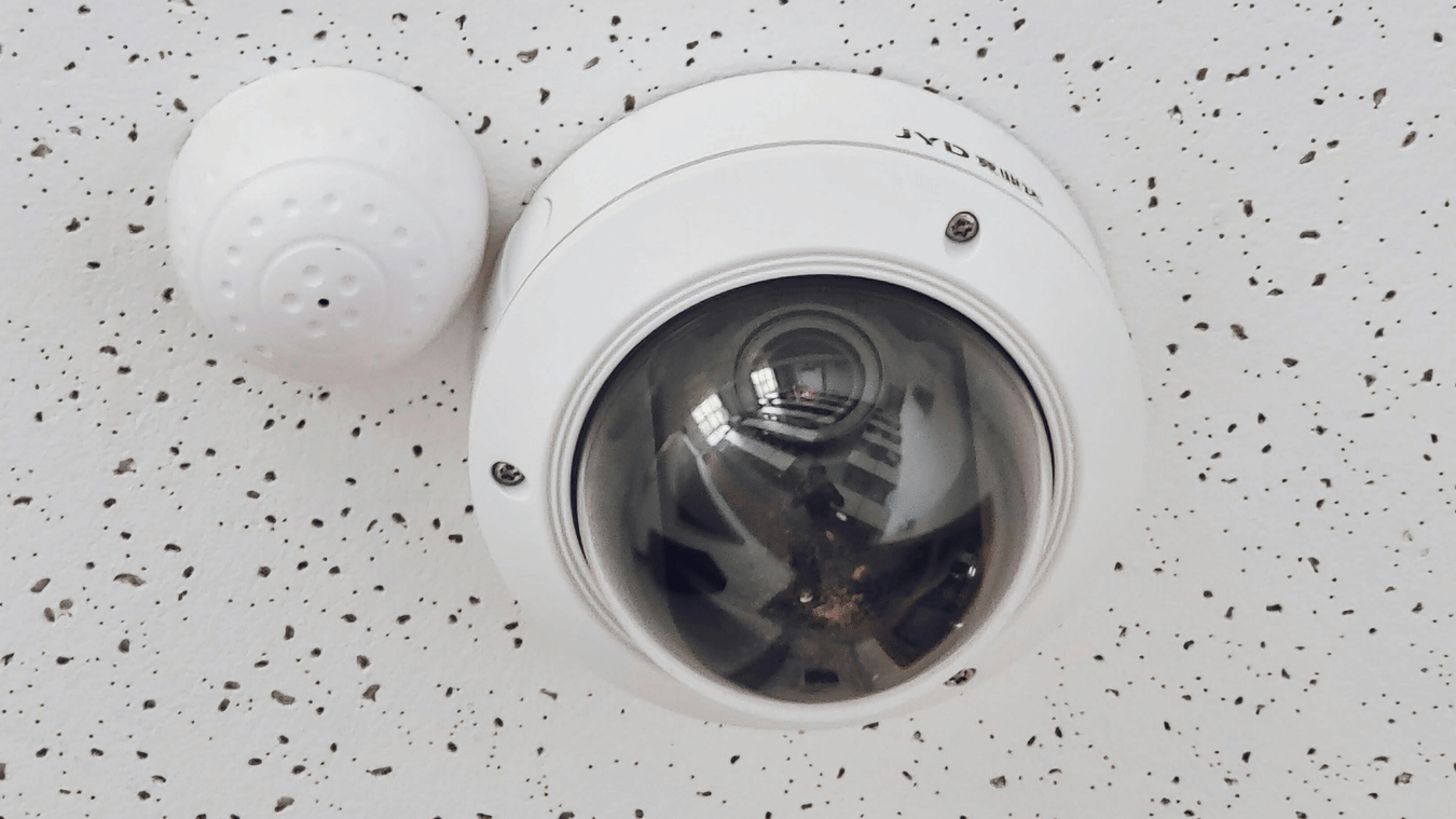 Dome security camera installed on a speckled white ceiling.