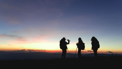 a group of people talking pictures while wearing their gear for hiking with the evening sky in the background