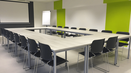Training room with long tables arranged in rows and green accent walls.