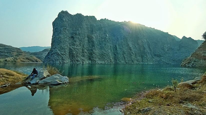 a large rock at a lake and a person is sitting the by the lake 
