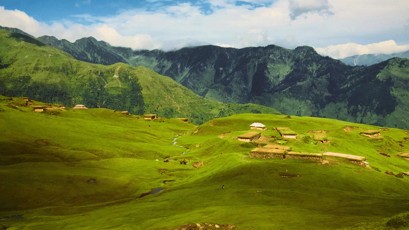 A large valley with forested hills in the background and green fields in the foreground.