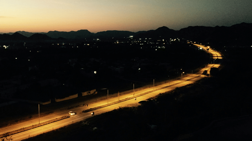 A highway at night shows vehicle light trails and illuminated surroundings.