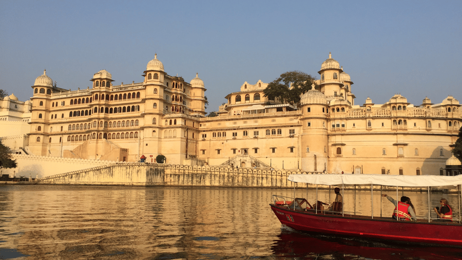 Udaipur City Palace beside the lake, with a boat carrying people travelling across the water.