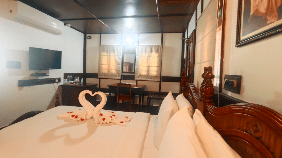 Elegantly decorated bed with swan towels and rose petals in a traditional wooden room at The Travancore Heritage Beach Resort, offering a romantic stay near Kovalam Beach.