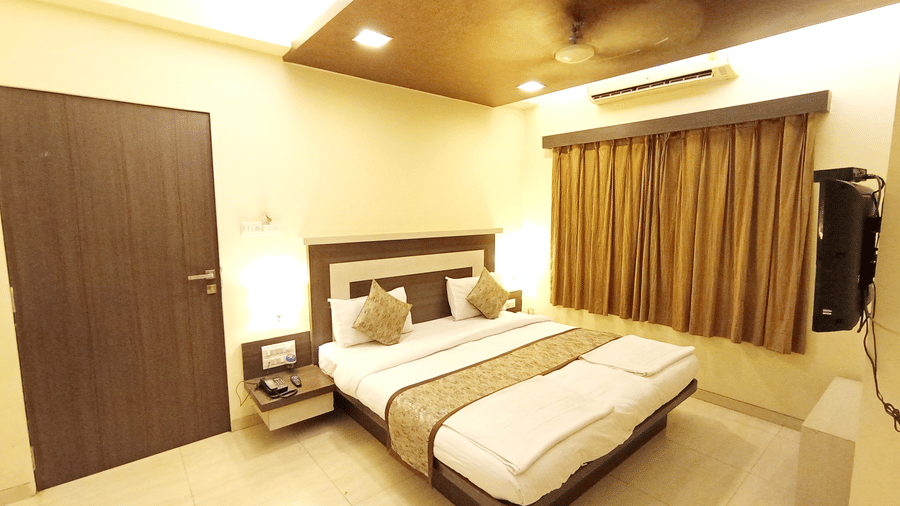executive room view displaying a dark wooden entrance door, a large double bed, and matching brown window drapes.