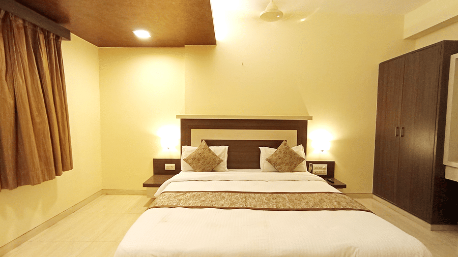 front view of executive room with a double bed, bedside lights, dark wardrobe, and elegant ceiling paneling.