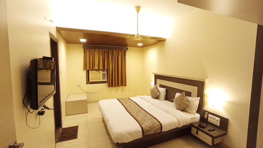 Executive room featuring a wall-mounted TV, a double bed with a brown runner, and a window with matching curtains.