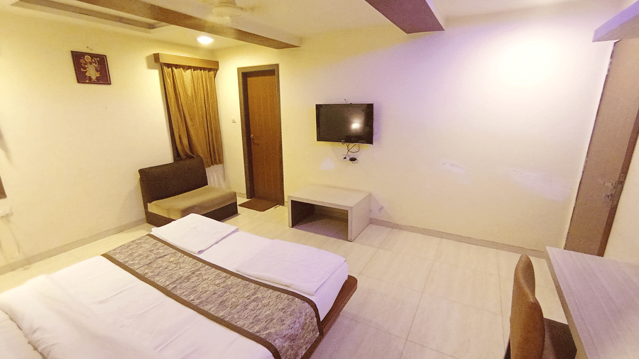Executive room with a double bed, writing desk with chair, wall television, and a separate seating stool.