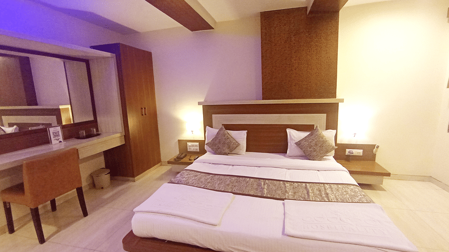 front view of a well-furnished suite room showcasing a double bed, wooden desk with a chair, and illuminated headboard.