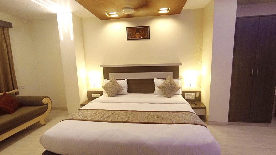 Suite room  with a double bed, warm bedside lamps, and a glimpse of a sofa seating area on the left.