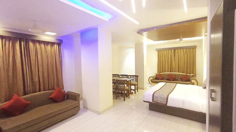 Suite room featuring bright linear ceiling lights, a brown couch, and a bed in the background.