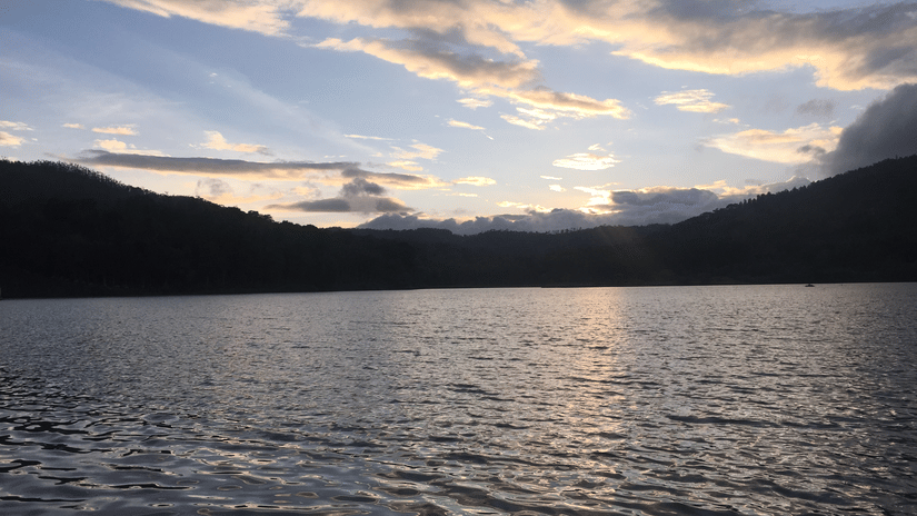 Calm lake surrounded by rolling hills under a colourful sunset sky, creating a peaceful and scenic landscape.
