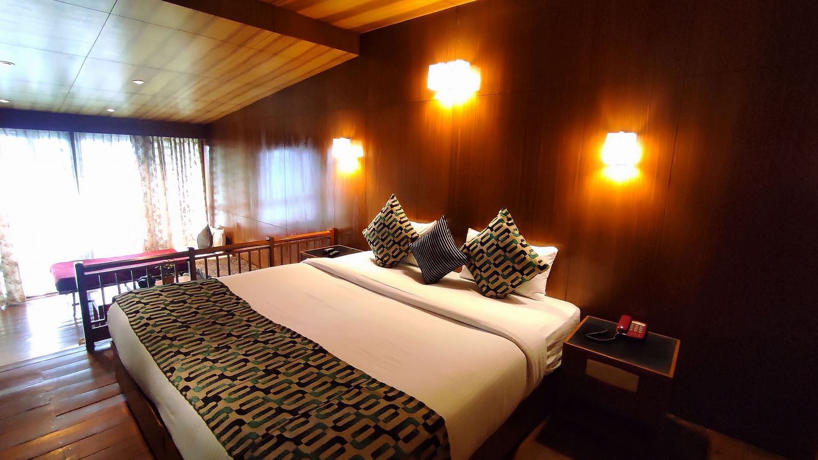 The Deluxe room of Cedar Inn, Darjeeling features a plush double bed with warm lighting, wooden interiors and a separate living area.