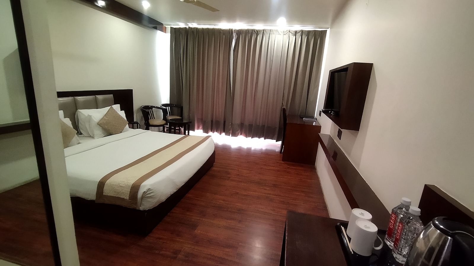 Another view of a modern hotel room with a large bed, a flat-screen TV and wooden flooring - TGI Apple Inn, Jaipur 