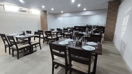 The dining hall at Perfectstayz Value Om Palace, Vrindavan, showing wooden tables with place settings under recessed ceiling lights.