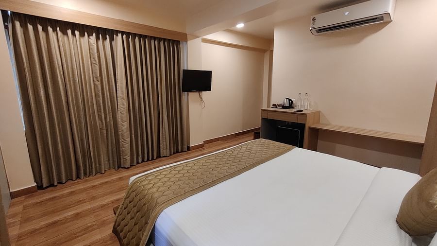 Bright bedroom featuring a king-sized bed, wooden furnishings, and large curtains