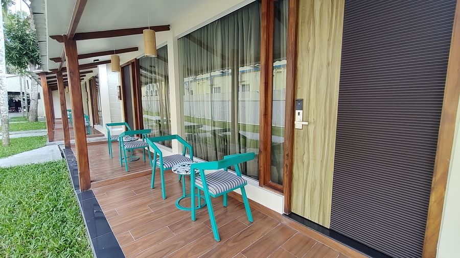 Outdoor patio with turquoise chairs overlooking a lush green lawn and glass doors - Arina Island Resort, Swaraj Dweep