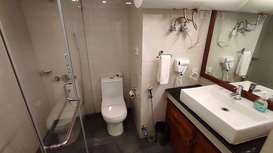 Bathroom at the Cedar Inn in Darjeeling featuring a white sink, a western commode, a mirror and a separate showering area.