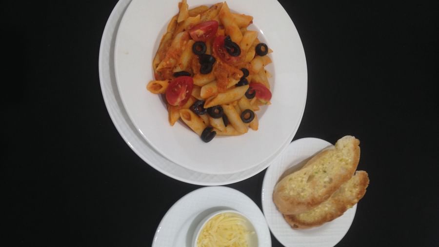 Pasta with black olives and a side of garlic bread and a yellow dip | Daksh The Madhuvan Suites