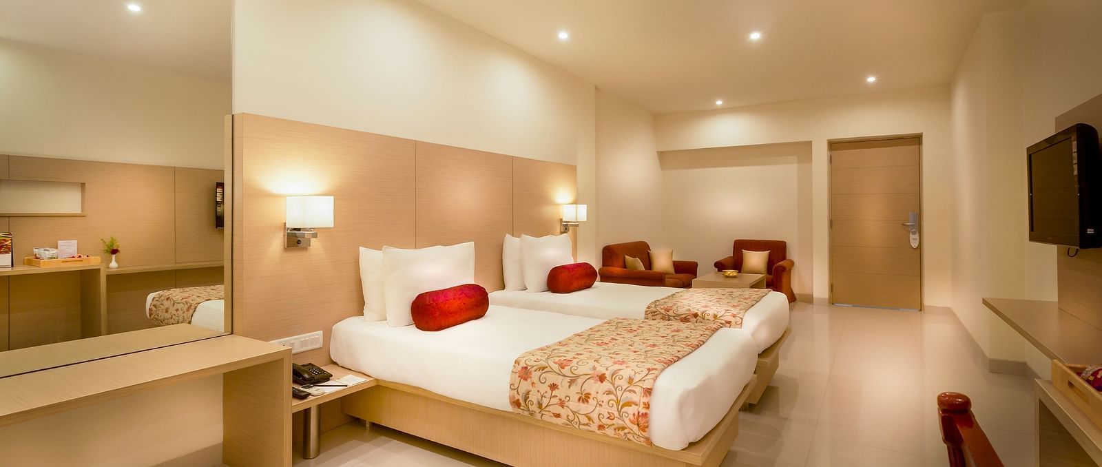 An image of a king size bed with a work desk and TV of a Suite at Regency Tiruttani by GRT Hotels.