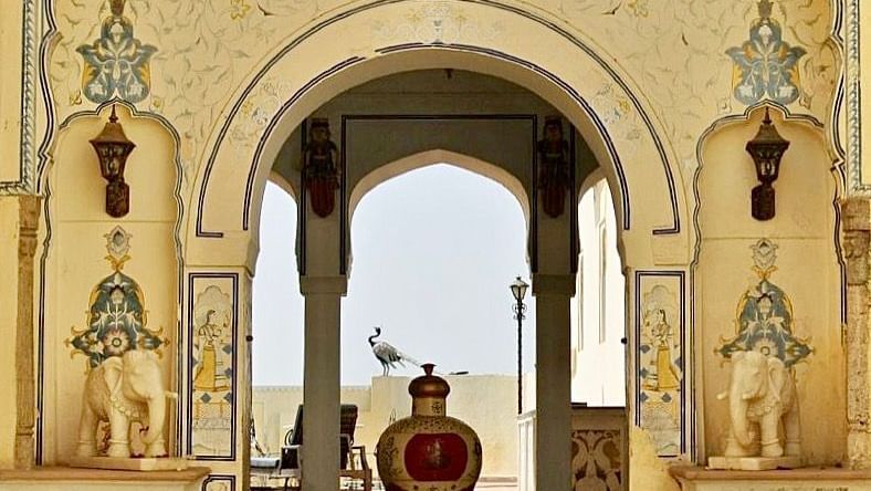 An ornately decorated archway frames a glimpse into an interior space at Fort Barli, showcasing intricate architectural details and a distant view.
