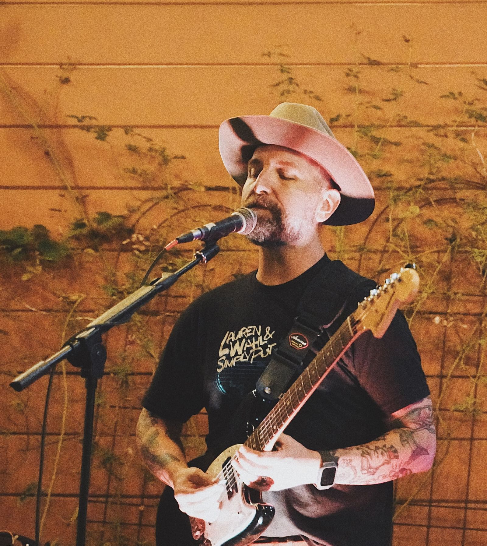 A person with a hat singing while playing the guitar - The Groveland Hotel.