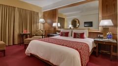 An image of Suite room featuring a double size bed, bedside table with lamp on either side, and a sitting area with sofa chair at Pride Sun Village Resort and Spa, Goa