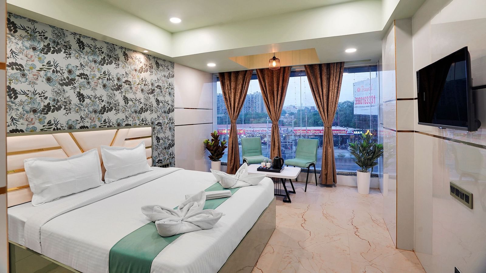 A king size bed in Deluxe Room with large windows overlooking the city at Hotel Regal Heaven, Pune.