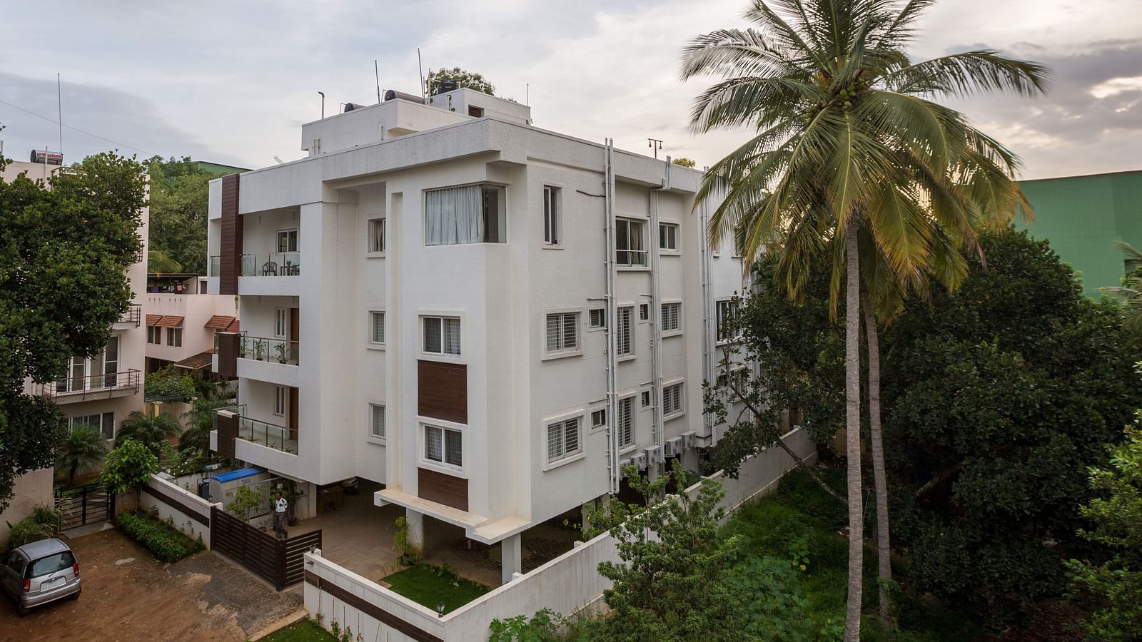 A light-coloured building exterior surrounded by green trees under a bright sky - Sanctum Suites BEL Road, Bangalore