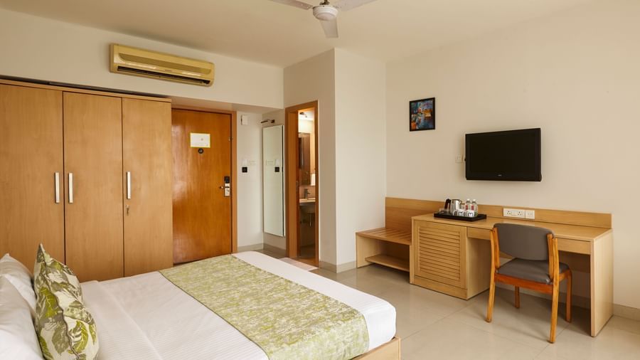 A tidy hotel room at Monday Hotels Mahape, Navi Mumbai, featuring a large bed, TV, and a desk.
