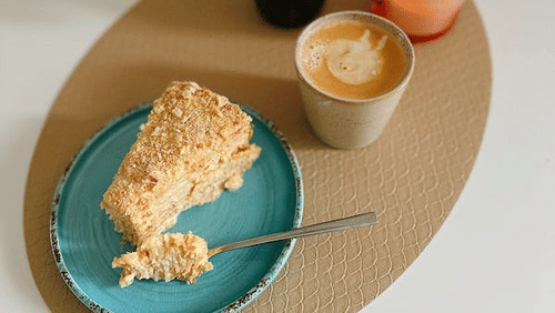 image featuring a sliced cake on a platter served with a small flower and a candle as well