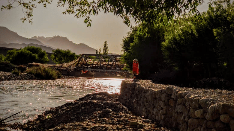 Bright sunlight filtering through leafy tree branches over a rocky riverbank at Indus Serenity Retreat.