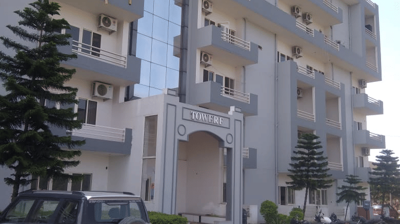 Exterior of the Livbox, Rudrapur featuring parked cars, balconies and lush green on both sides of the driveway.