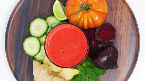 A beverage served on a wooden plate with fresh tomato, cucumber, beetroot, ginger, lime, and mint leaves arranged around at YO1 Longevity & Health Resorts.