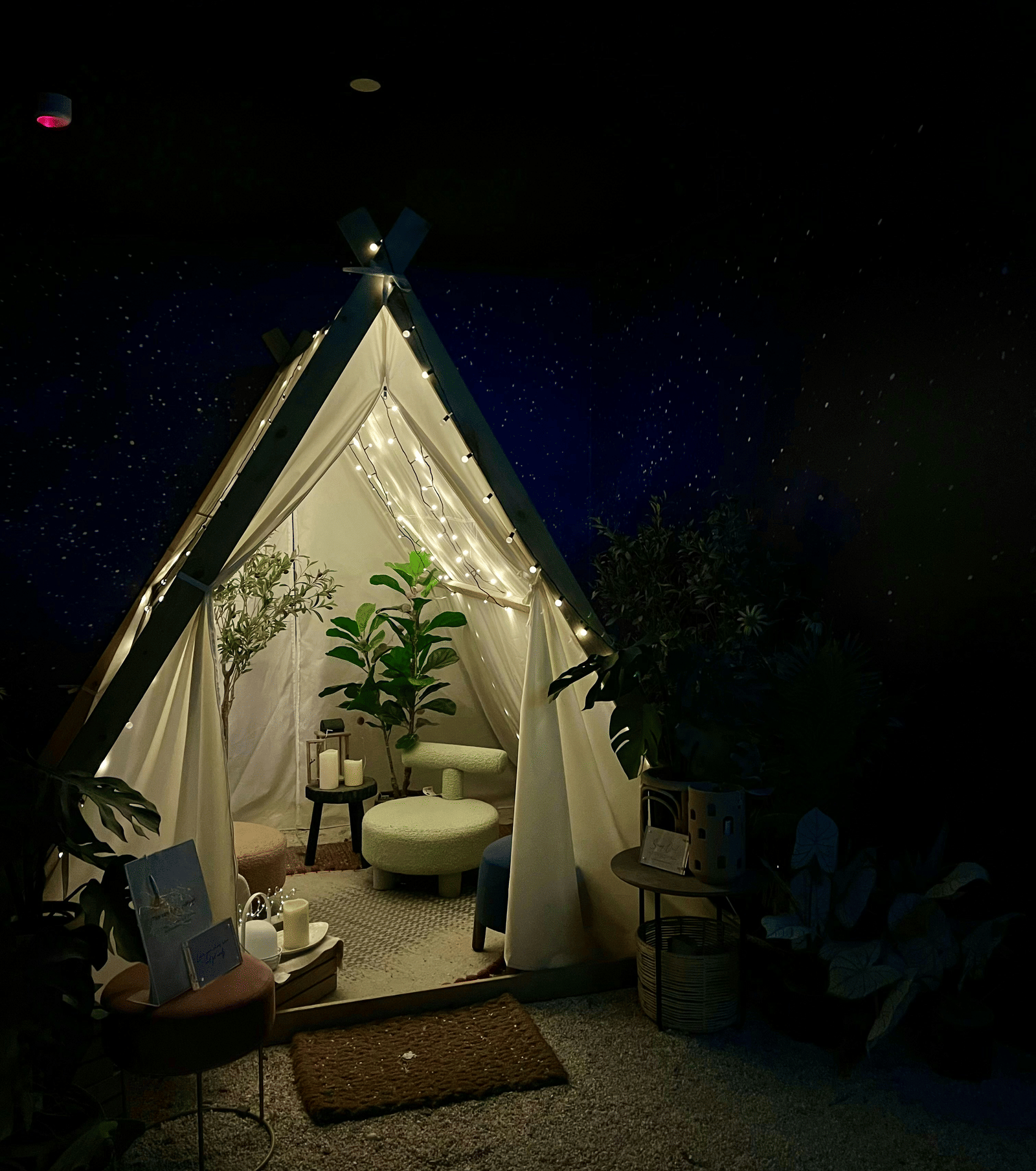 An outdoor view of a glamping tent at night, with a small table and chair set up on a porch in front.