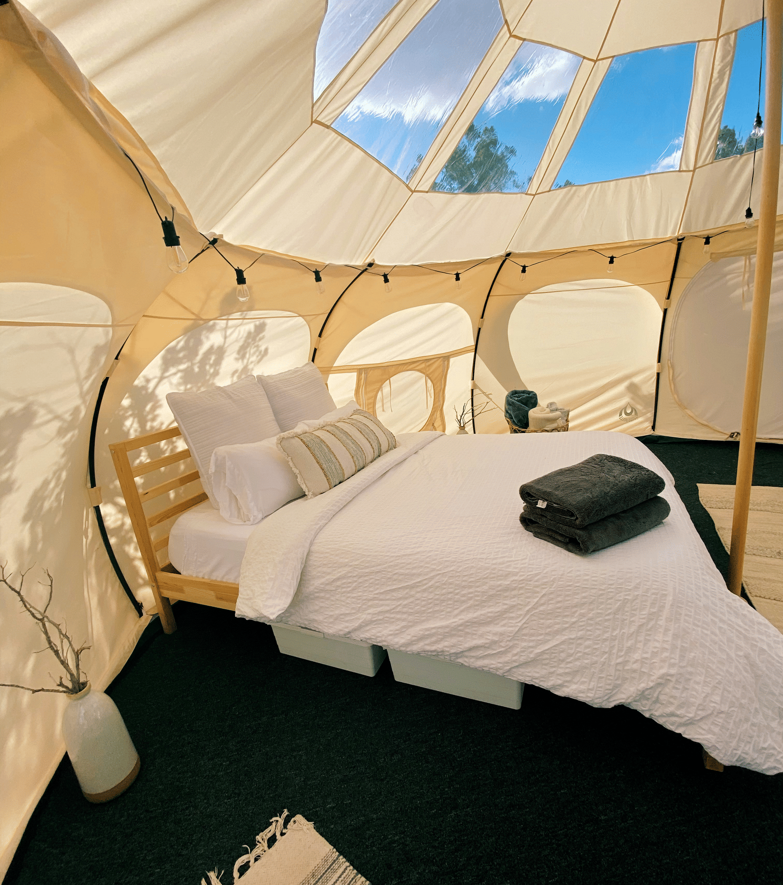 The interior of a modern glamping tent with a bed, chairs, and a window in the ceiling to view the sky.