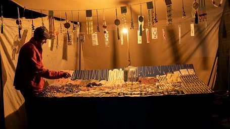 A man selling jewellery in a market under warm lights.