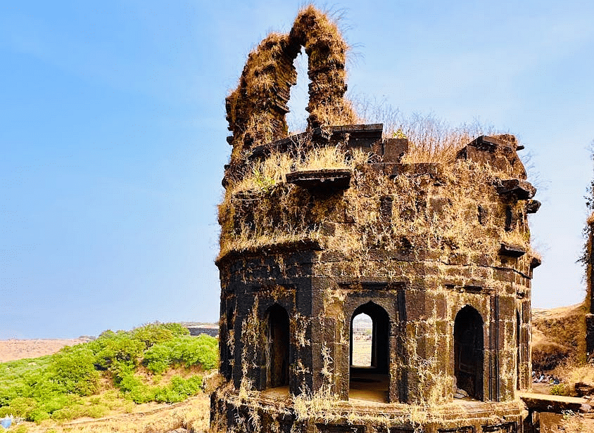 A weathered stone tower standing on a cliff side, overlooking the bright blue sky and ocean
