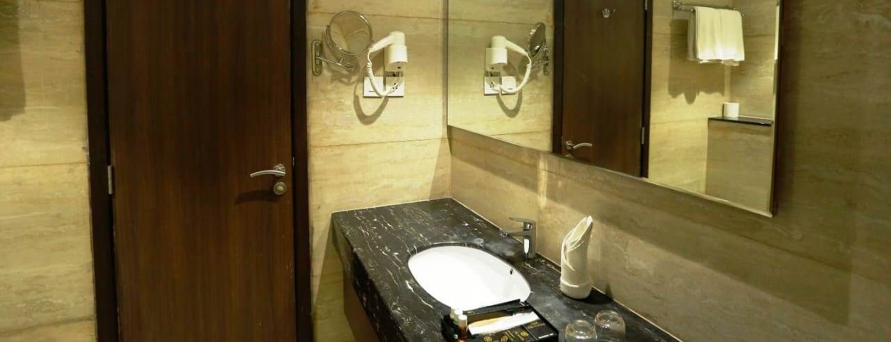 A bathroom with a single faucet, a mirror, and a wall-mounted blow dryer at The Hamuse Hotel, Kodaikanal