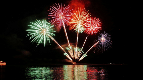 A far out view of fireworks in the distance on the sky with its reflection on the waterbody in view